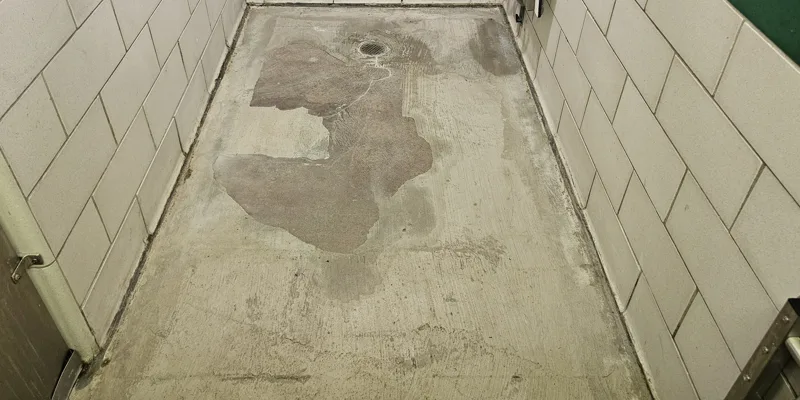 Patchy failed resurfacer on a bathhouse concrete floor around an existing drain