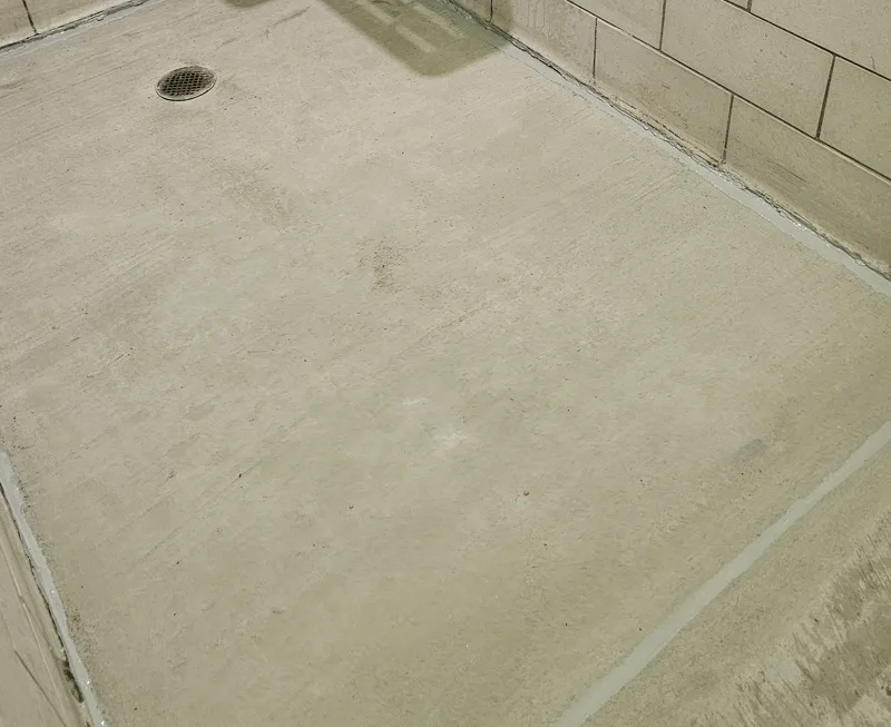Resurfaced bathhouse concrete floor around a retained drain with visible light joint sealing